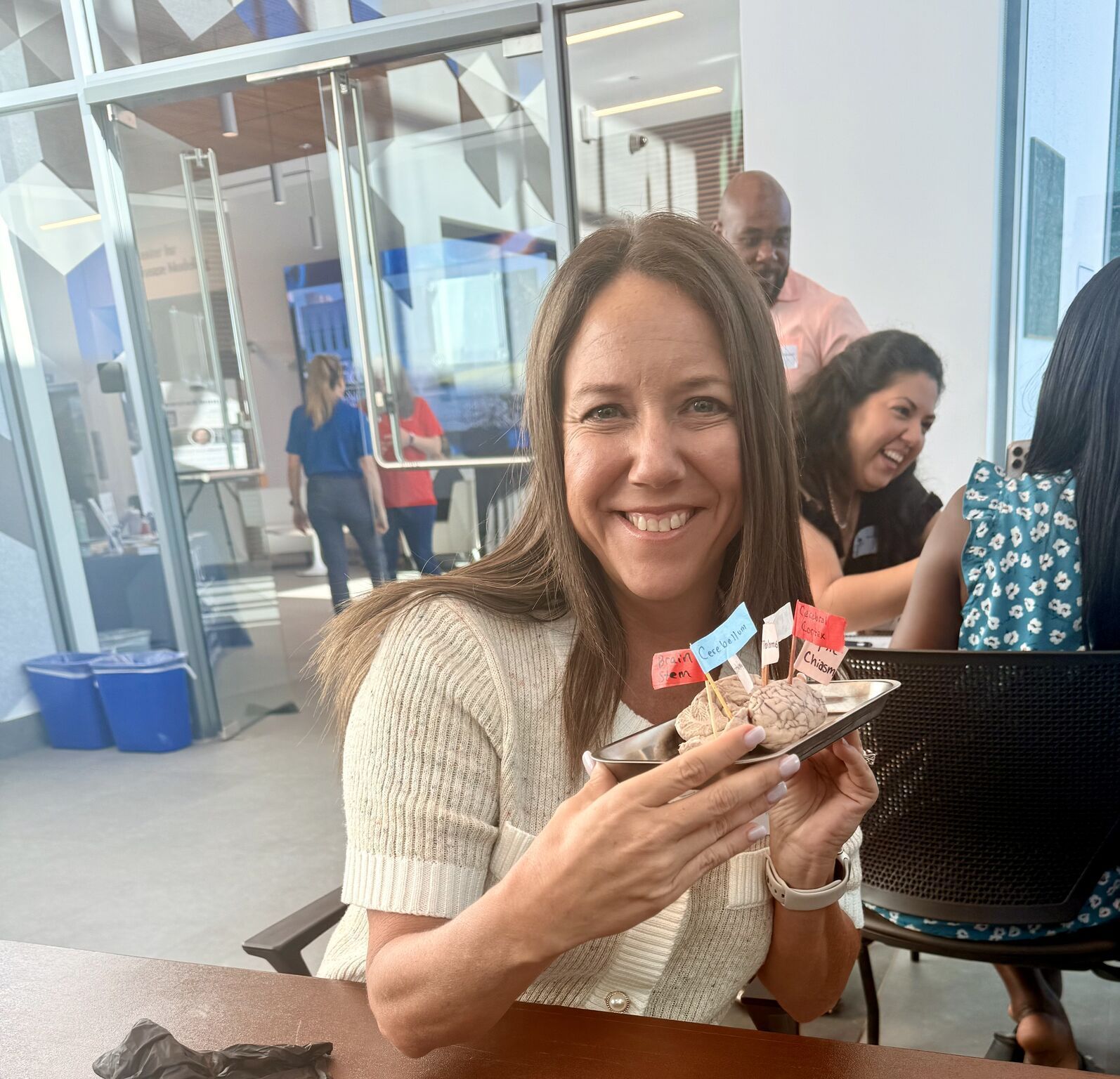 Woman smiles, holding plate of food decorated with flags at a gathering. Others in background.