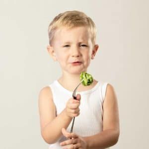A young boy is holding a fork with a piece of lettuce on it.