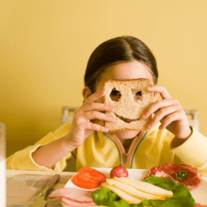 A little girl is covering her face with a piece of bread with a smiley face on it.