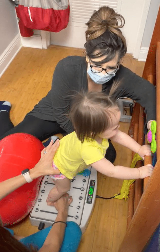 A woman wearing a mask is playing with a baby in a room.