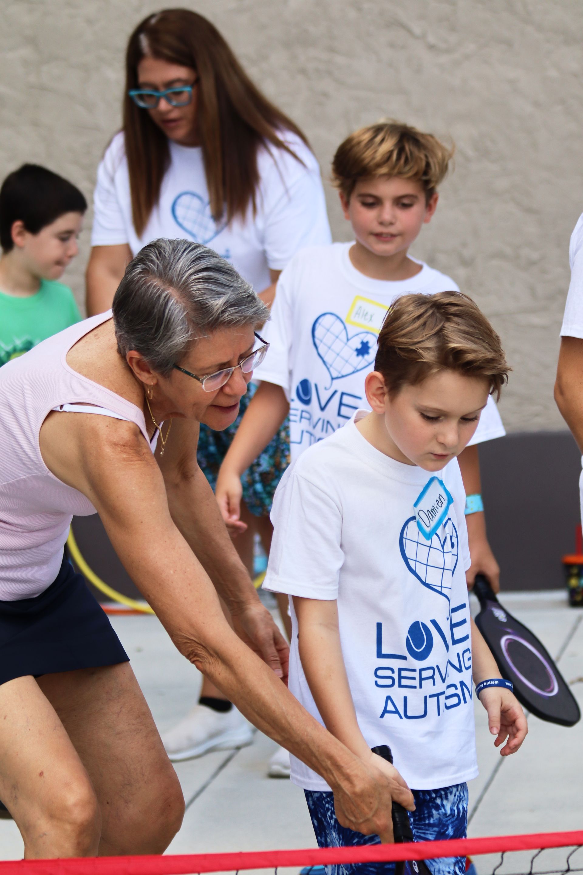 A woman is helping a young boy with a tennis racket.