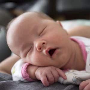 A baby is sleeping on a bed with its mouth open.