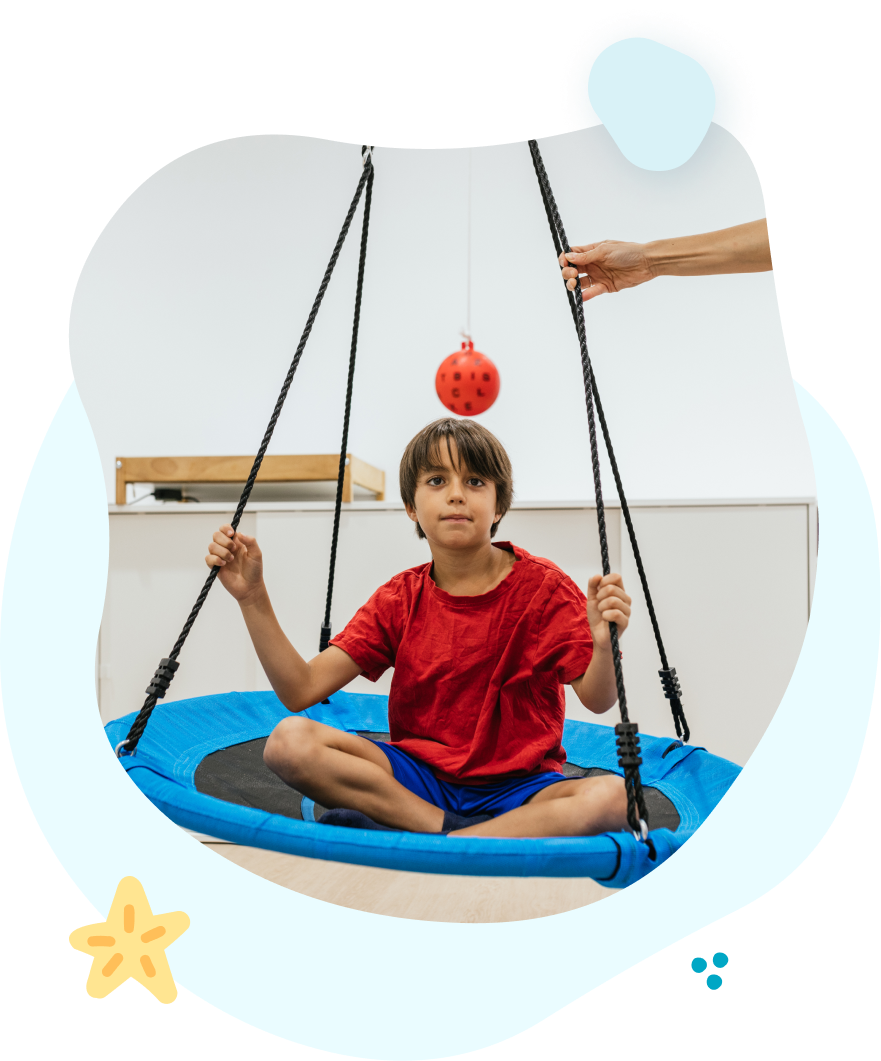 A boy is sitting on a blue swing with a ball on his head.