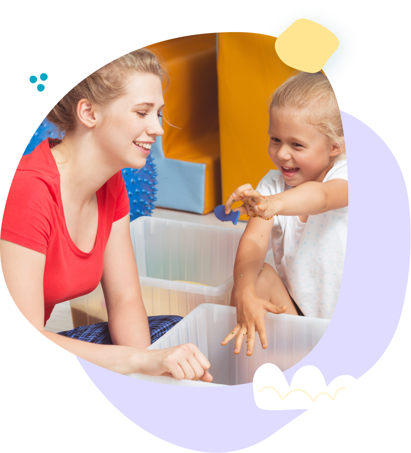 A woman is playing with a child in a sensory bin.