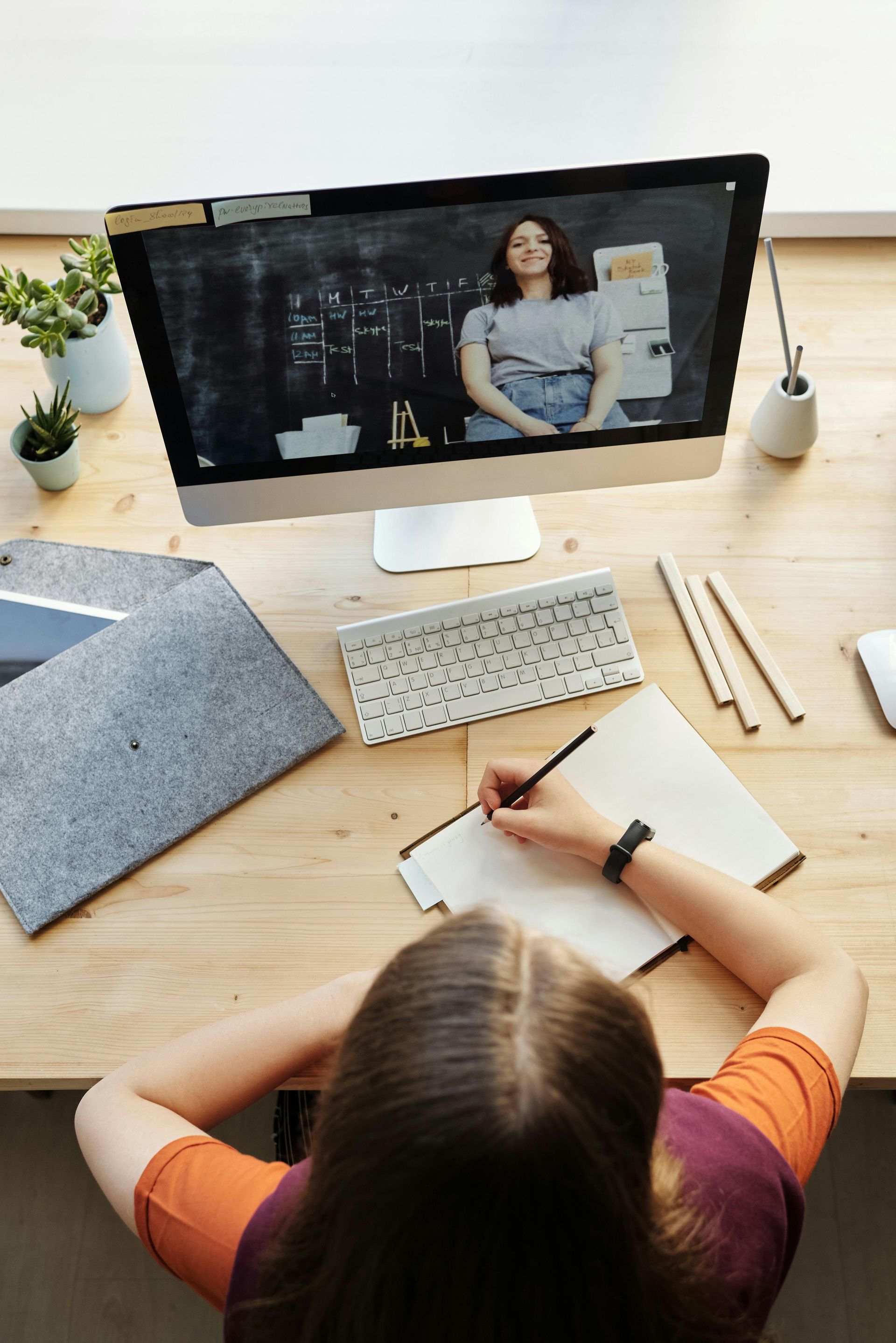 A woman is sitting at a desk using a computer and writing in a notebook.