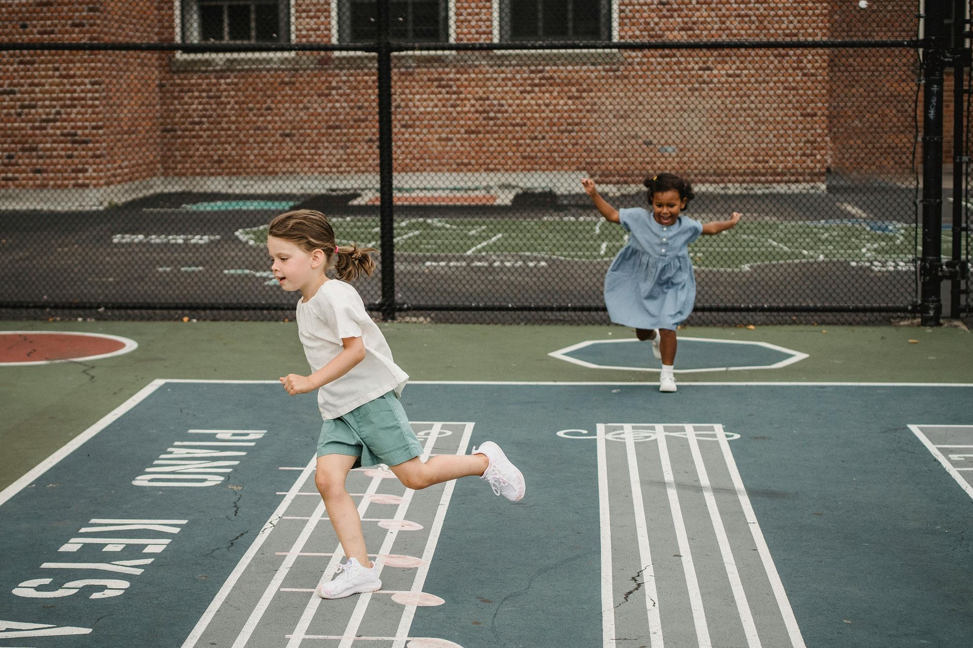 Two little girls are running on a basketball court.