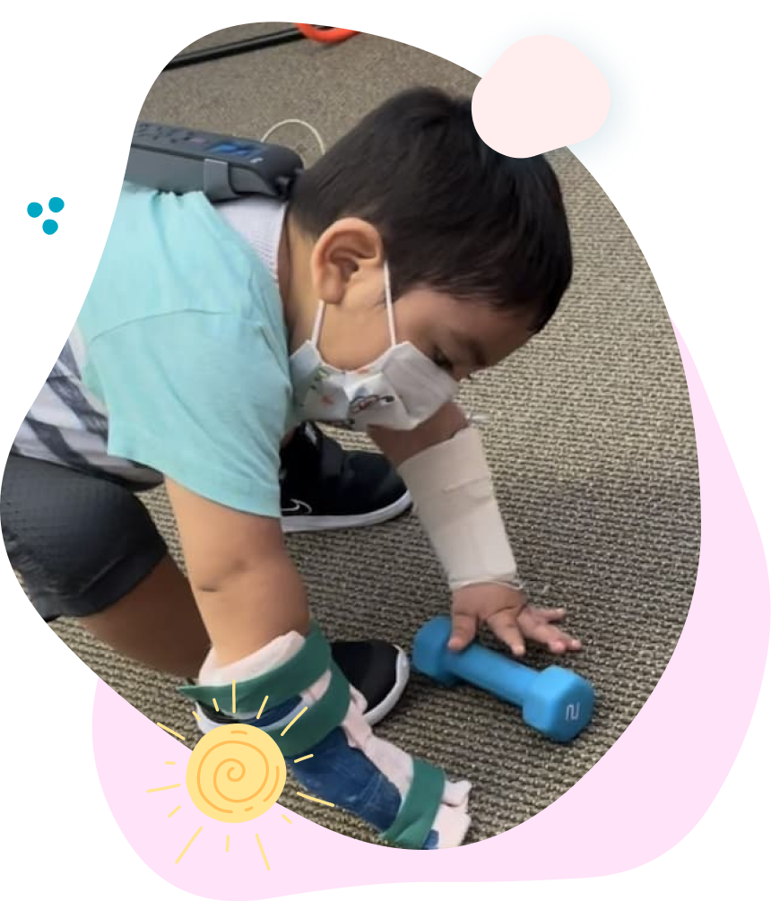 A young boy wearing a mask is playing with a blue dumbbell.