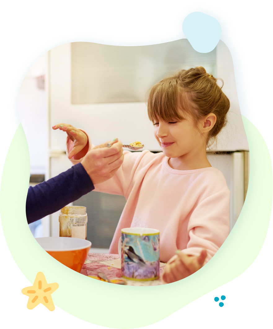 A little girl is sitting at a table with a spoon in her hand