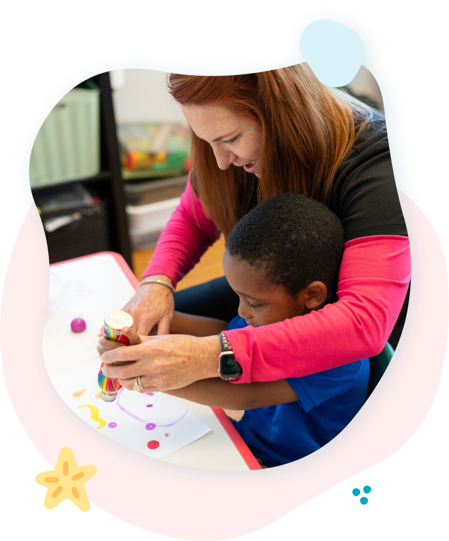 A woman is teaching a young boy how to use glue