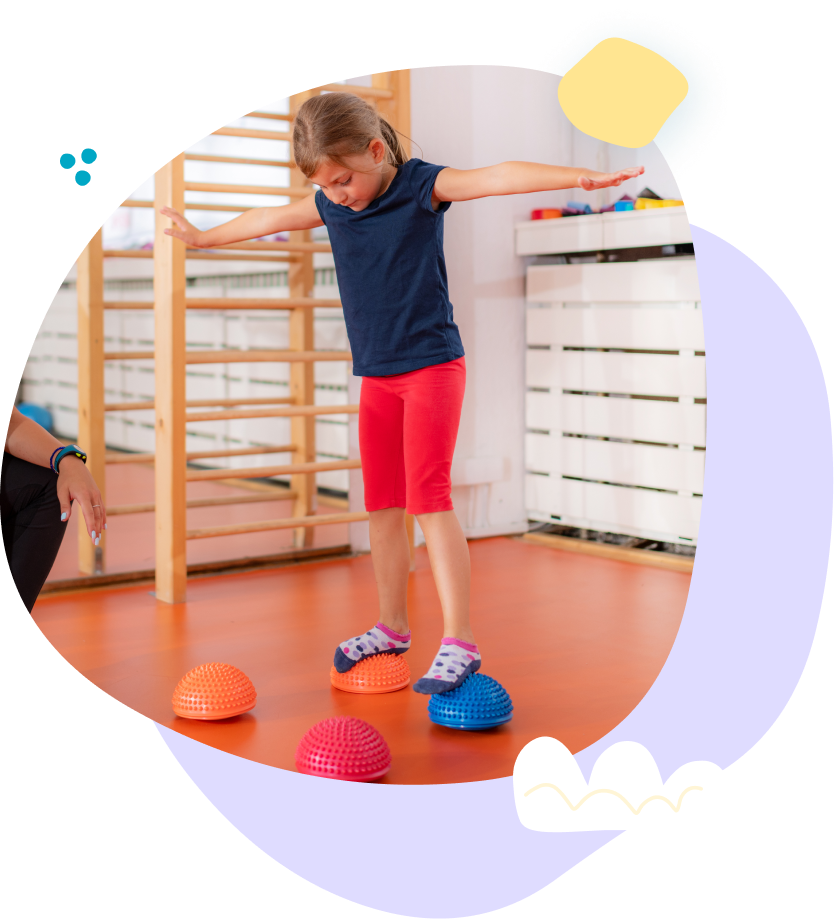 A little girl is standing on a balance ball in a gym.