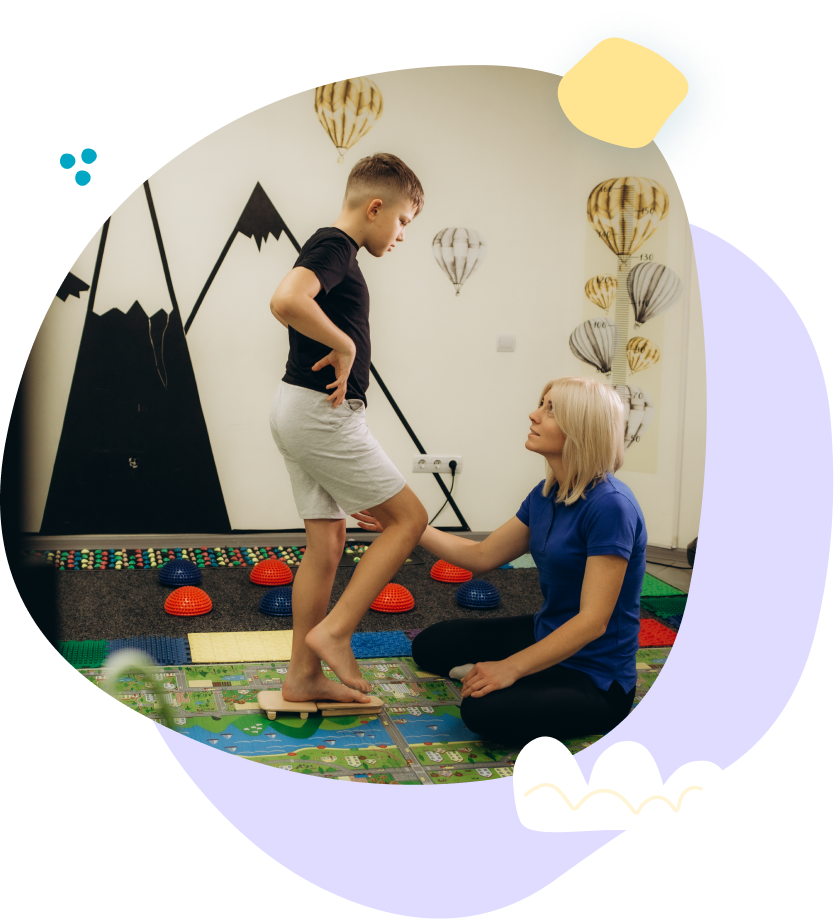 A woman is helping a young boy balance on a balance board