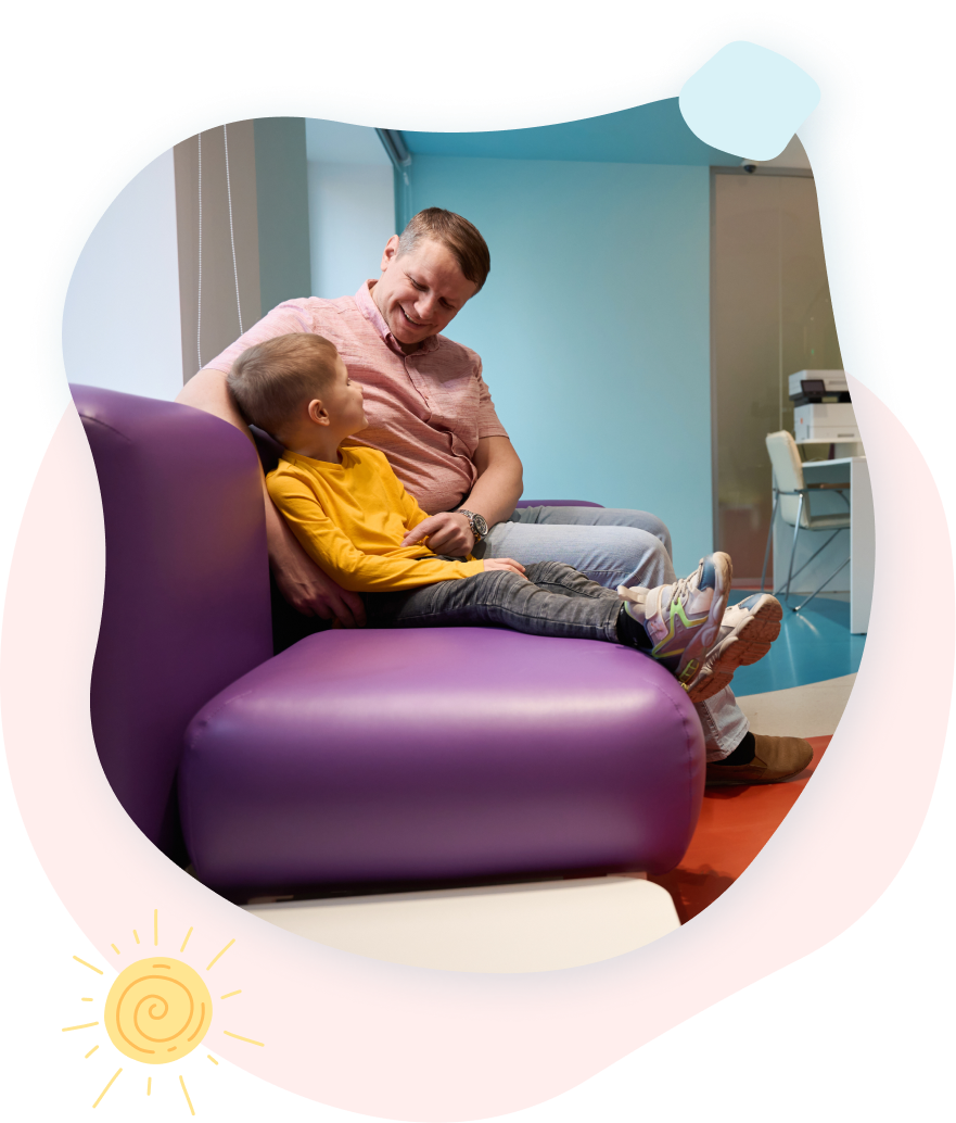 Smiling child at blue table with person; activity in brightly lit room.