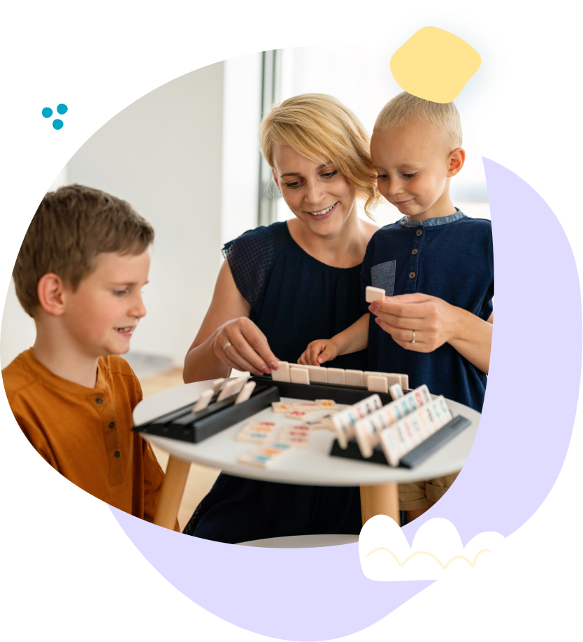 A woman and two children are sitting at a table playing a game.