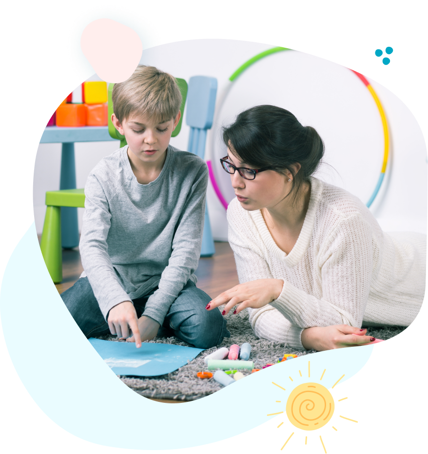 A woman and a boy are sitting on the floor playing with chalk.
