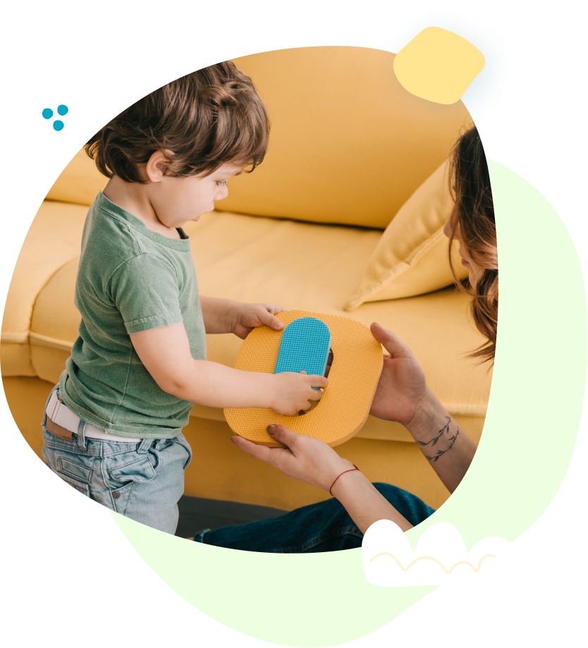 A woman is holding a toy in front of a toddler.