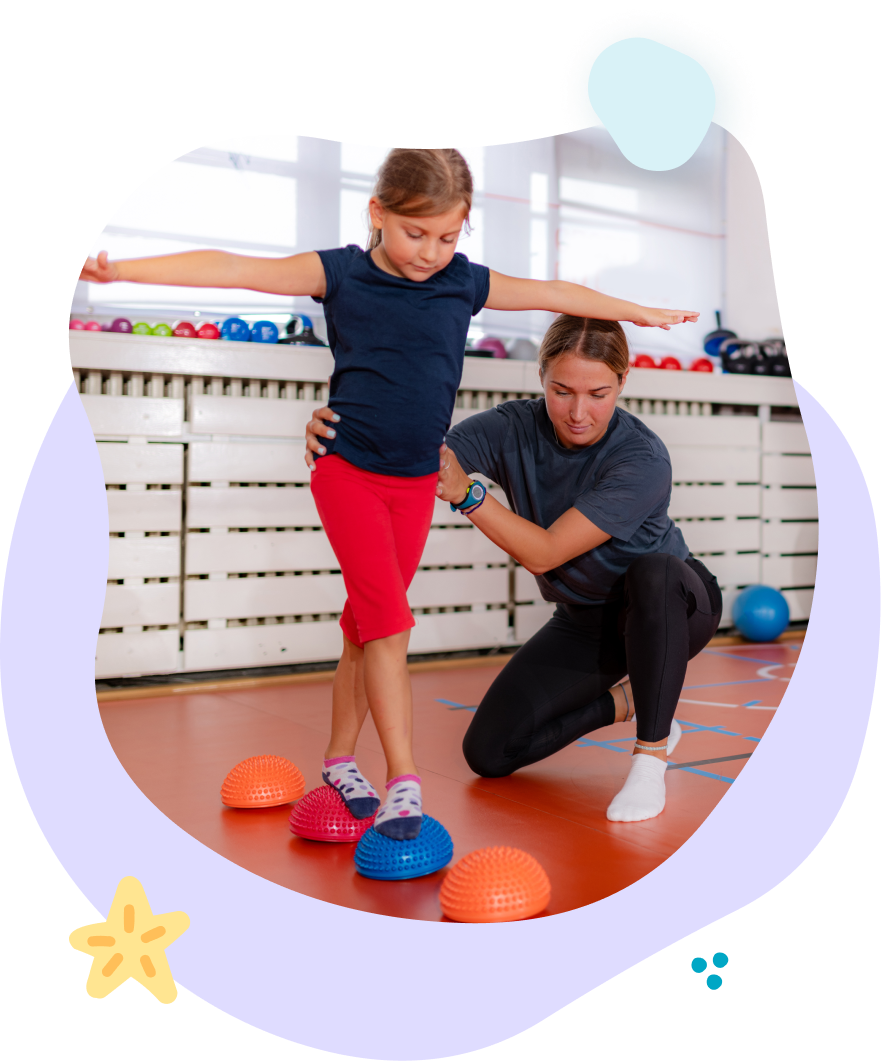 A woman is helping a little girl balance on a balance ball.