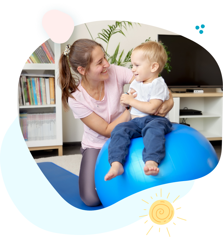 A woman is kneeling down next to a toddler sitting on a blue exercise ball.