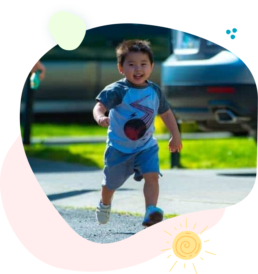 Smiling child runs towards the viewer on a paved path in front of a car.