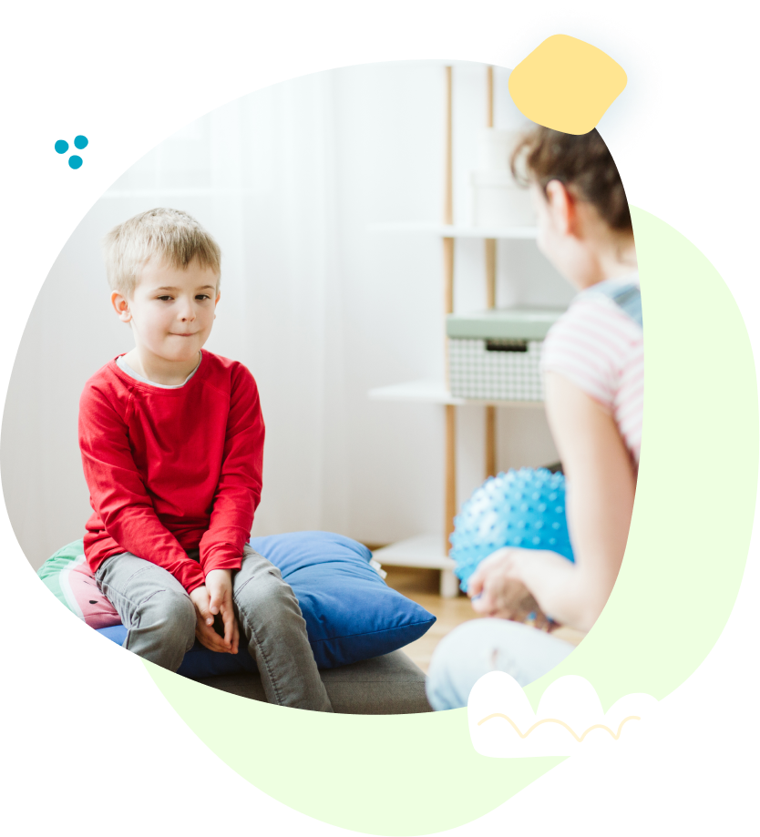 A young boy is sitting on a couch talking to a woman.