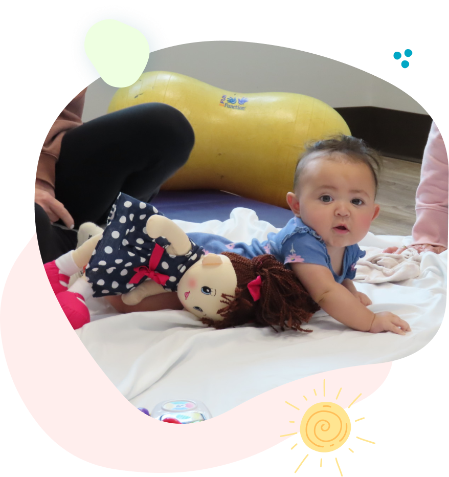 Baby in pink jumpsuit, pink bow, lying on a blanket, hands assisting.