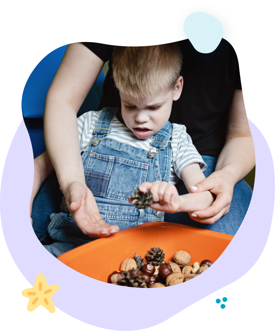 A little boy is playing with a bowl of pine cones.