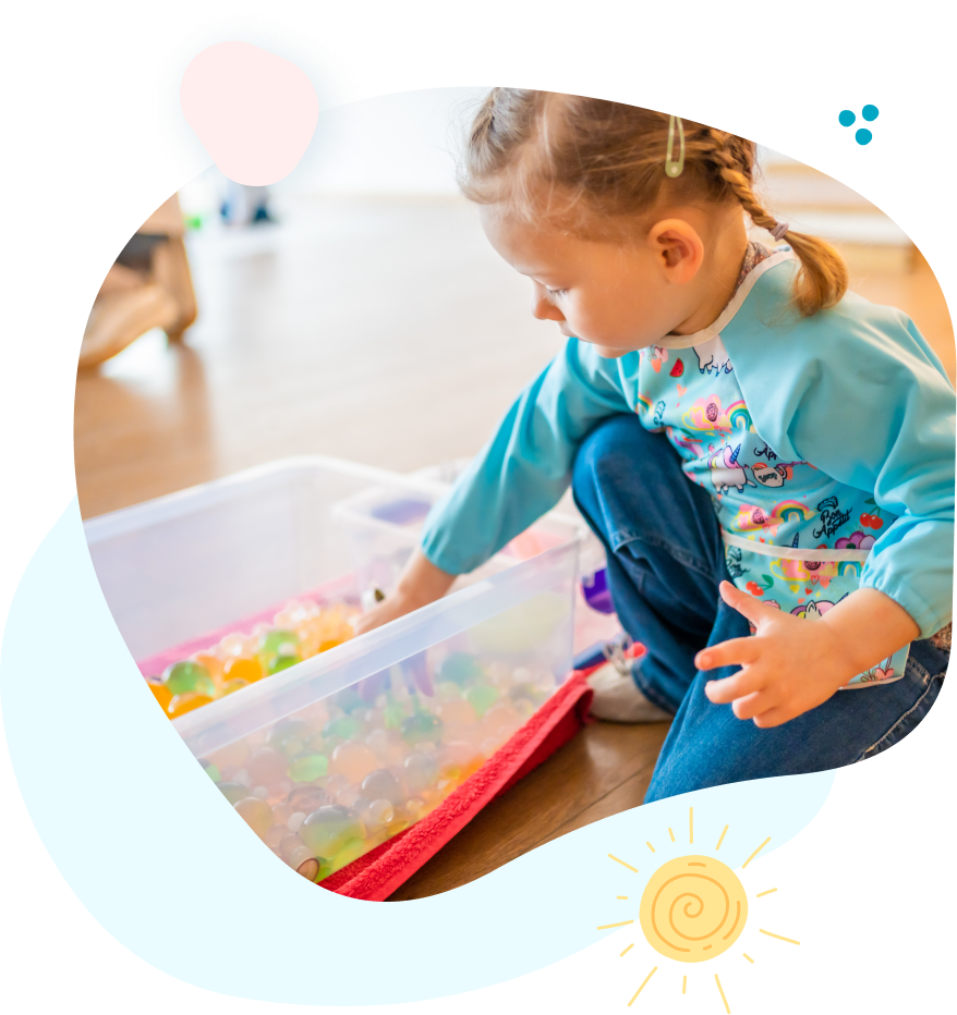 A little girl is playing with a box of toys on the floor.