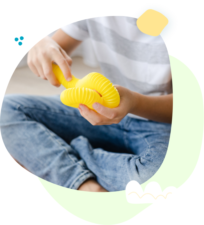 A child is sitting on the floor playing with a yellow slinky toy.