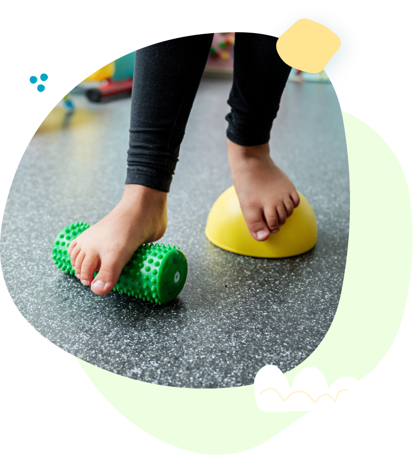 A child 's feet are standing on a green roller and a yellow ball.