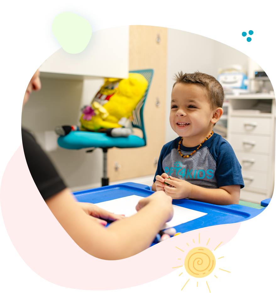 Smiling child at blue table with person; activity in brightly lit room.