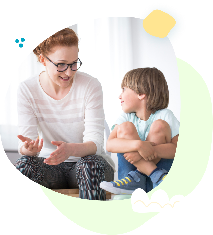 A woman and a boy are sitting on the floor talking to each other.