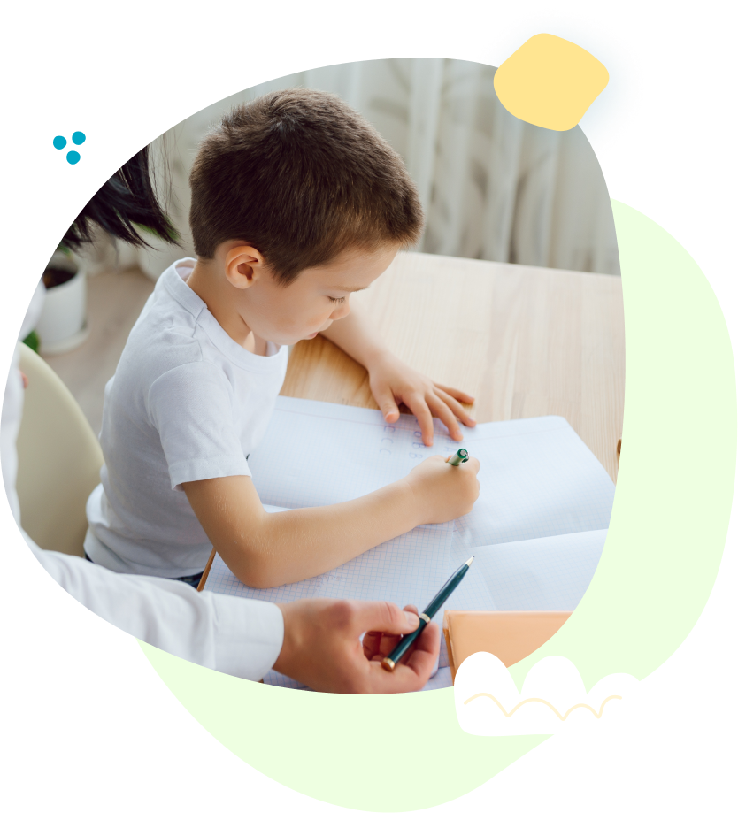 A young boy is sitting at a table writing in a notebook.