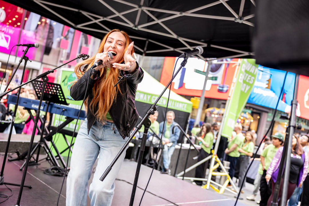 A high-energy Broadway performer singing into a microphone on the Times Square stage