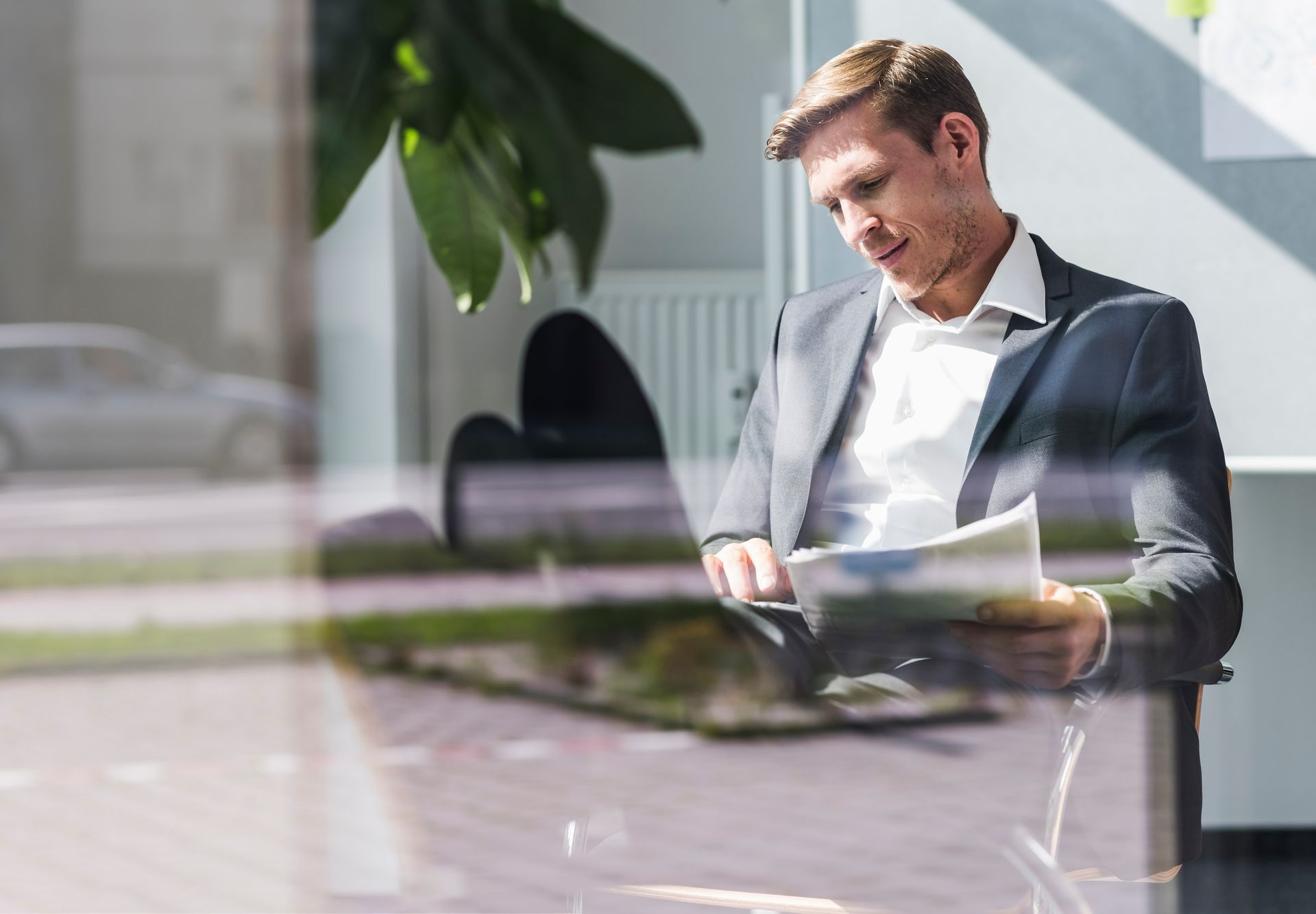 A person in a business suit sits, looking down and reviewing documents in a bright, modern office setting.