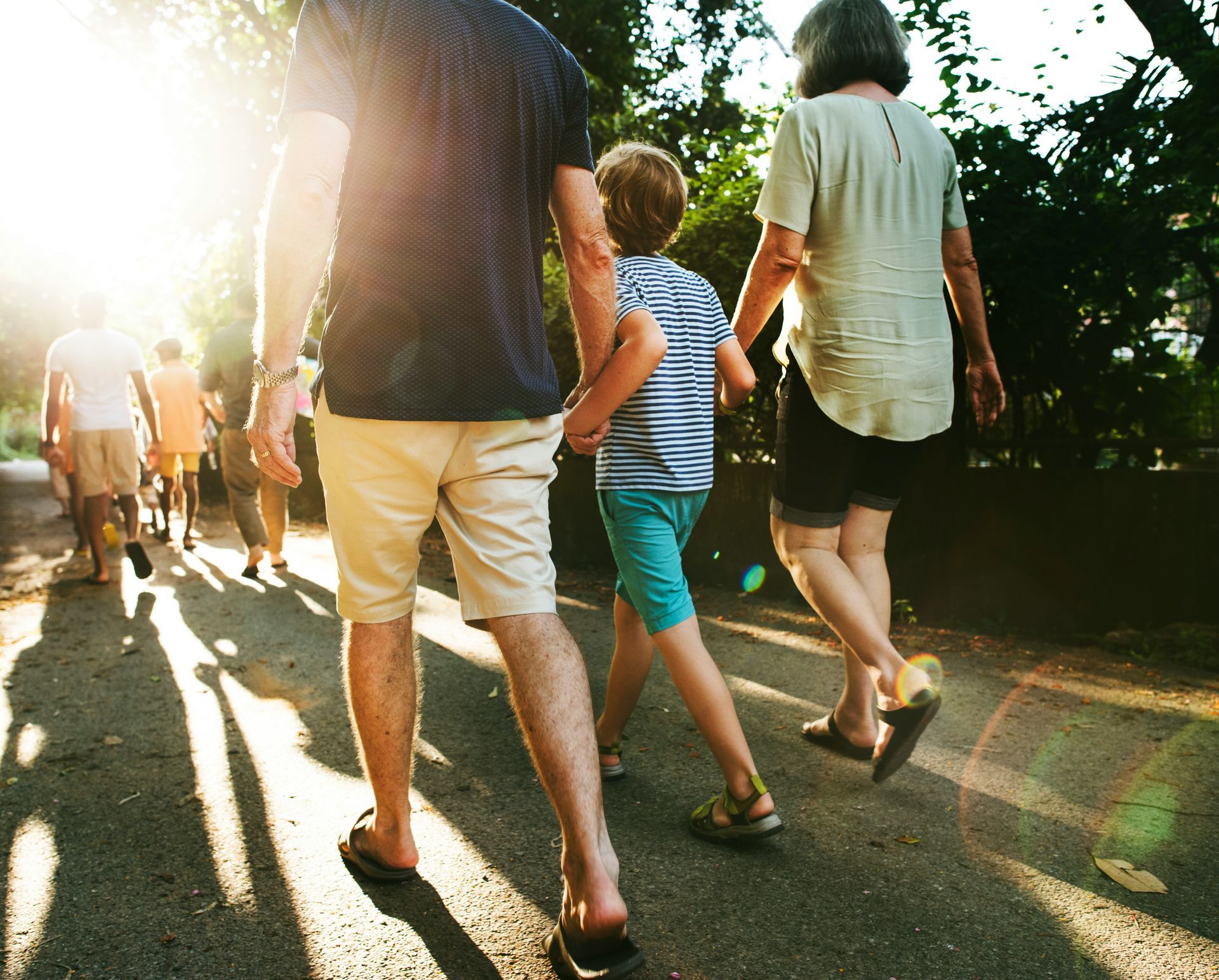 A family walks together on a sunlit outdoor path, viewed from behind.