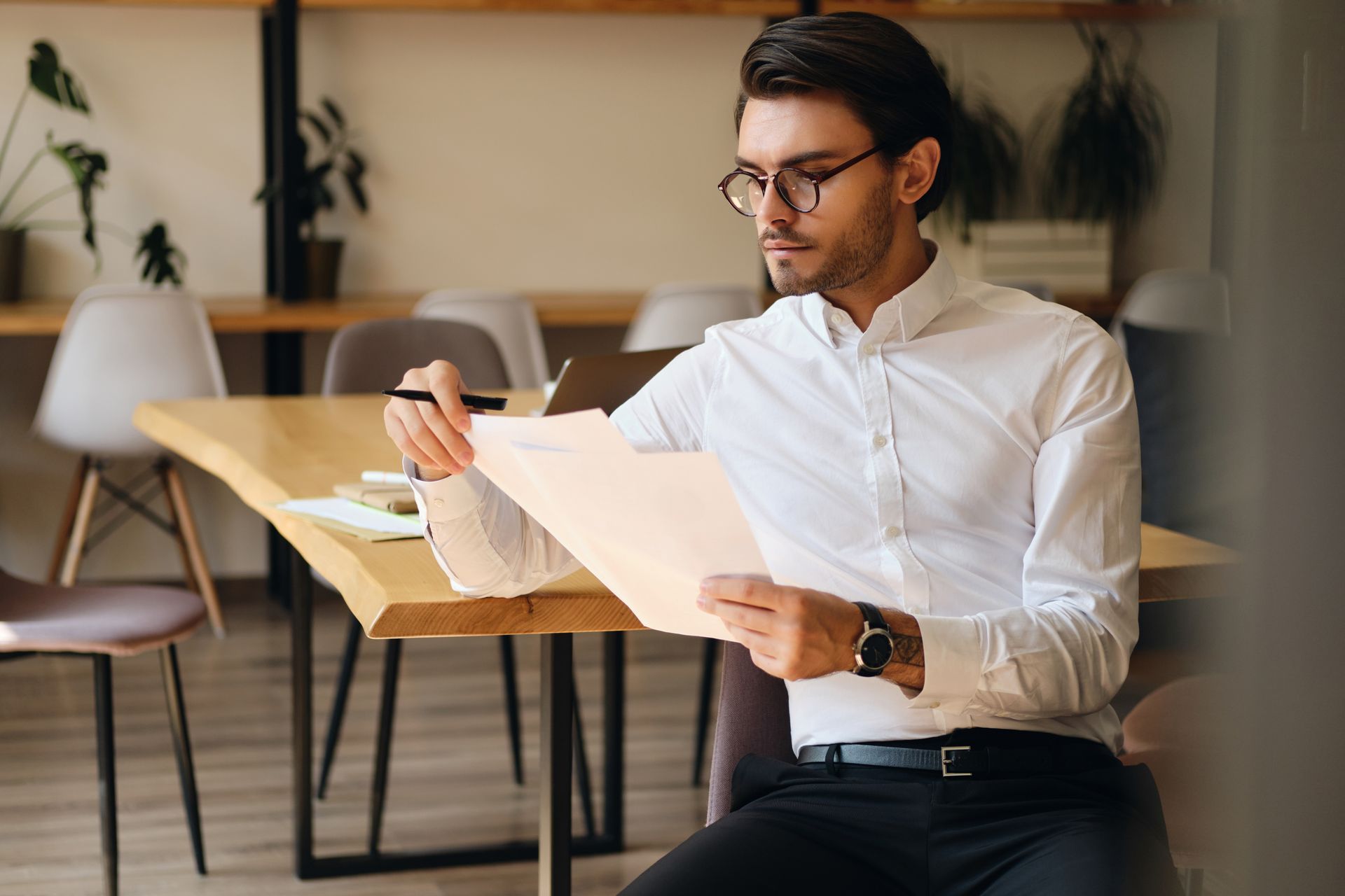 A person in a white button-down shirt and glasses sitting at a table and reviewing a document.