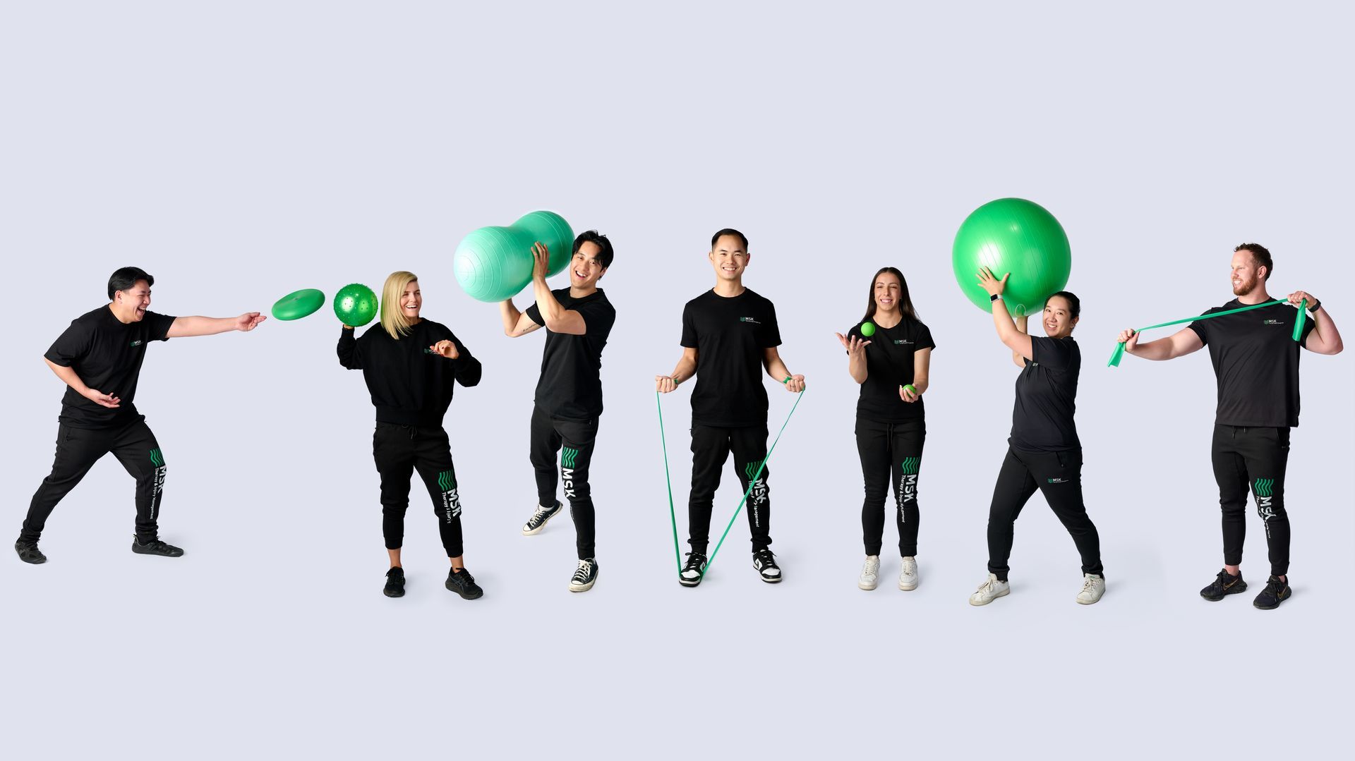 A group of people are standing in a row holding green exercise balls.