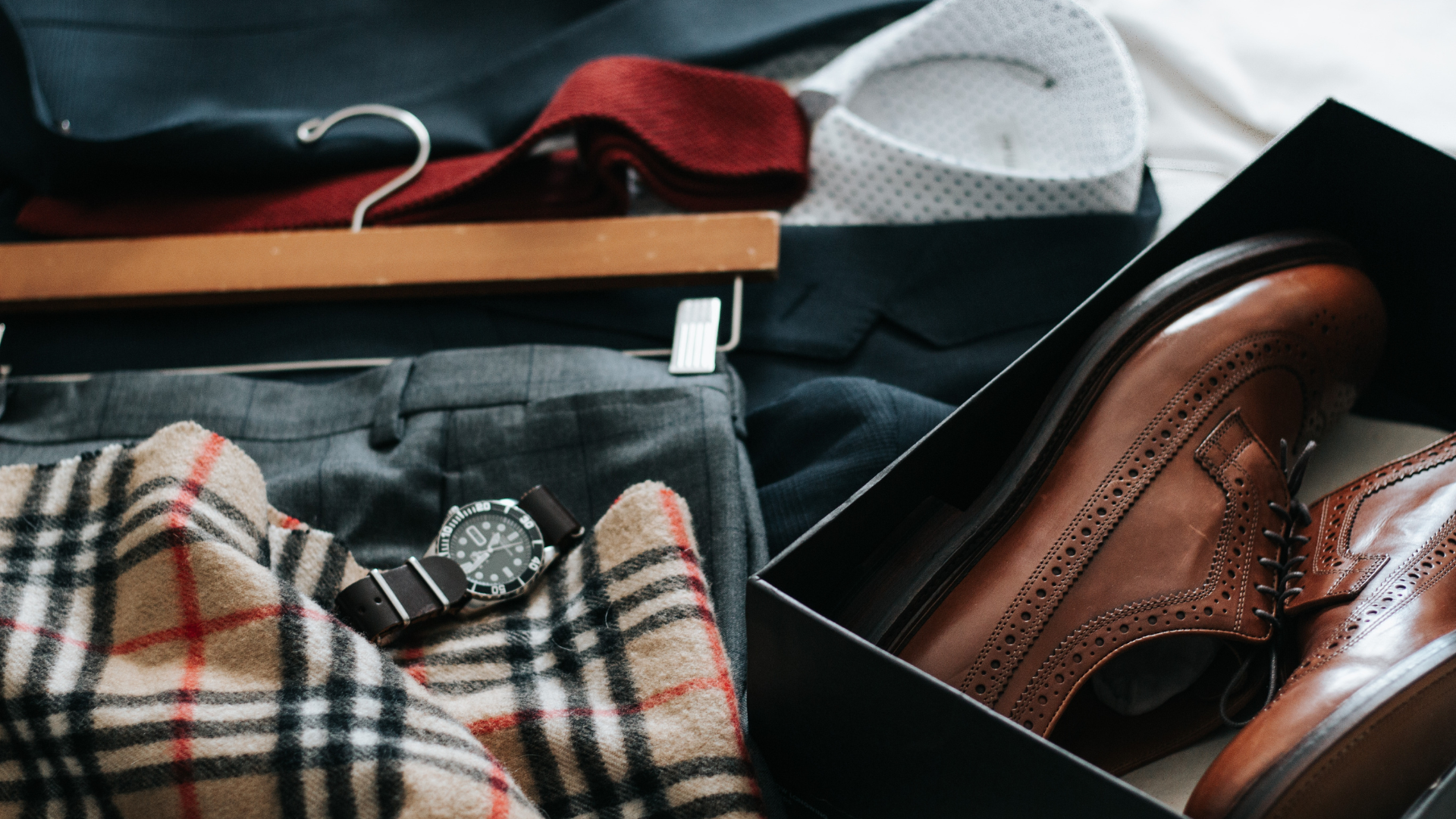 A suitcase filled with clothes and a pair of brown shoes.