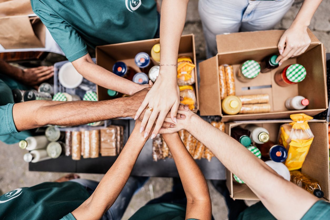 A group of people putting their hands together in front of boxes of food.