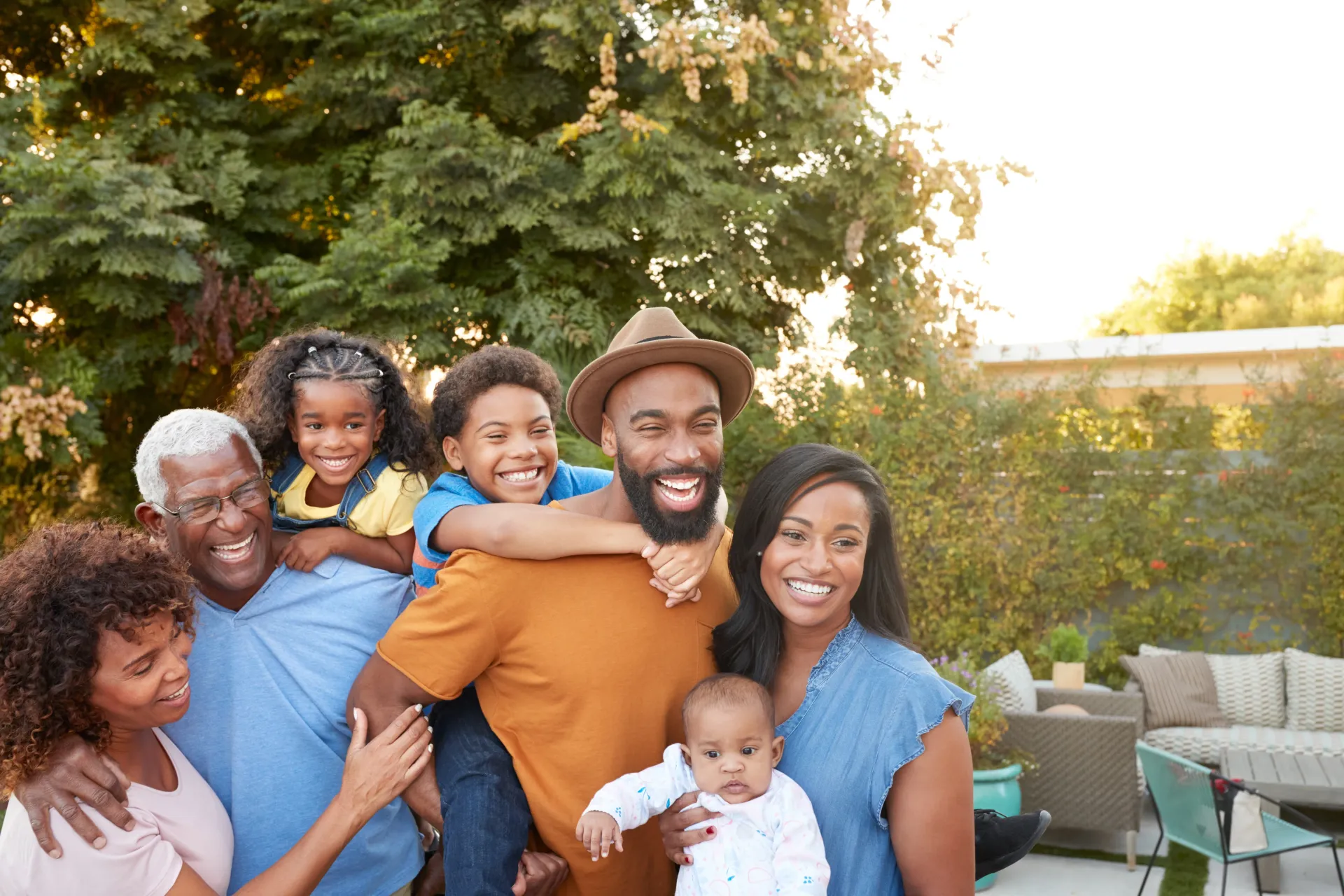 Multi-generational Black family smiling together outdoors; sunny.