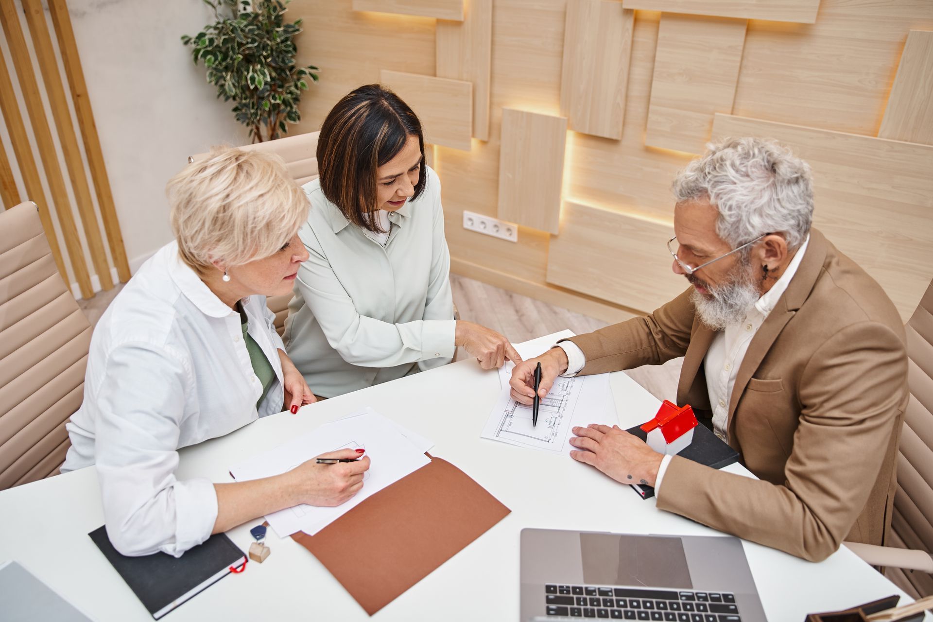 Three people in a meeting; senior man with grey beard points at papers, women on either side.