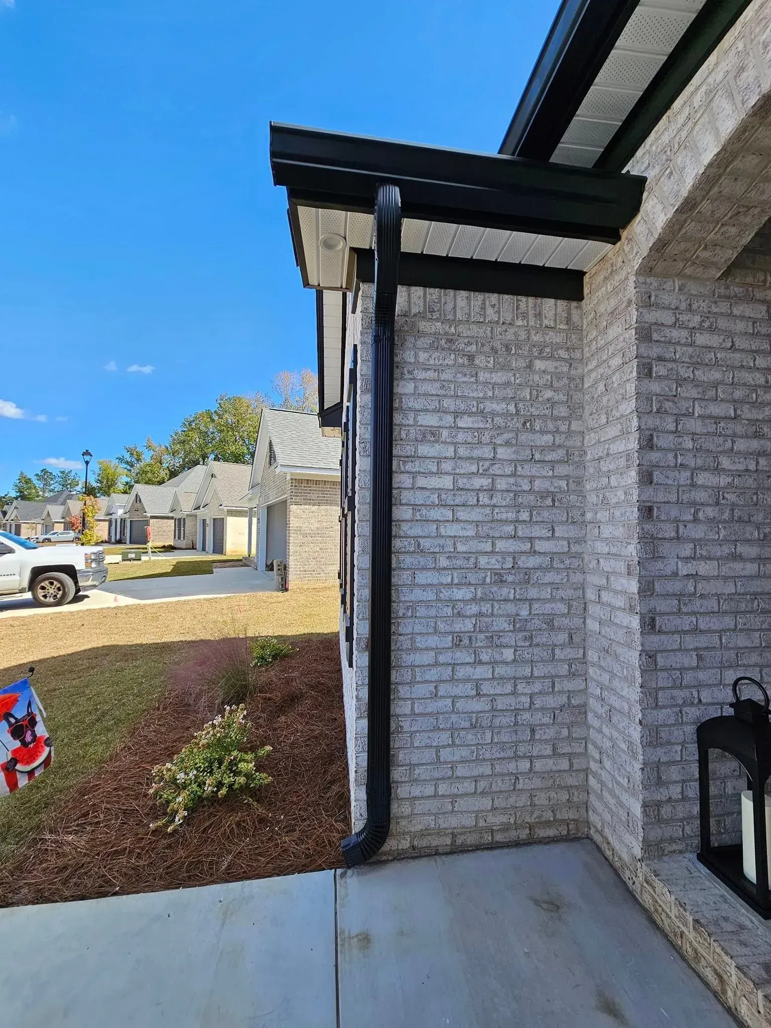 A white brick house with a black gutter on the side of it.