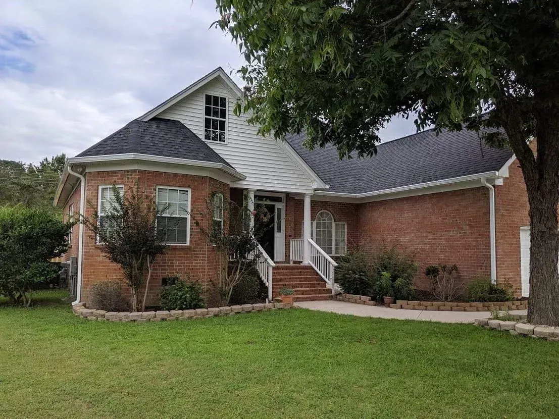 A brick house with a gray roof and a tree in front of it.