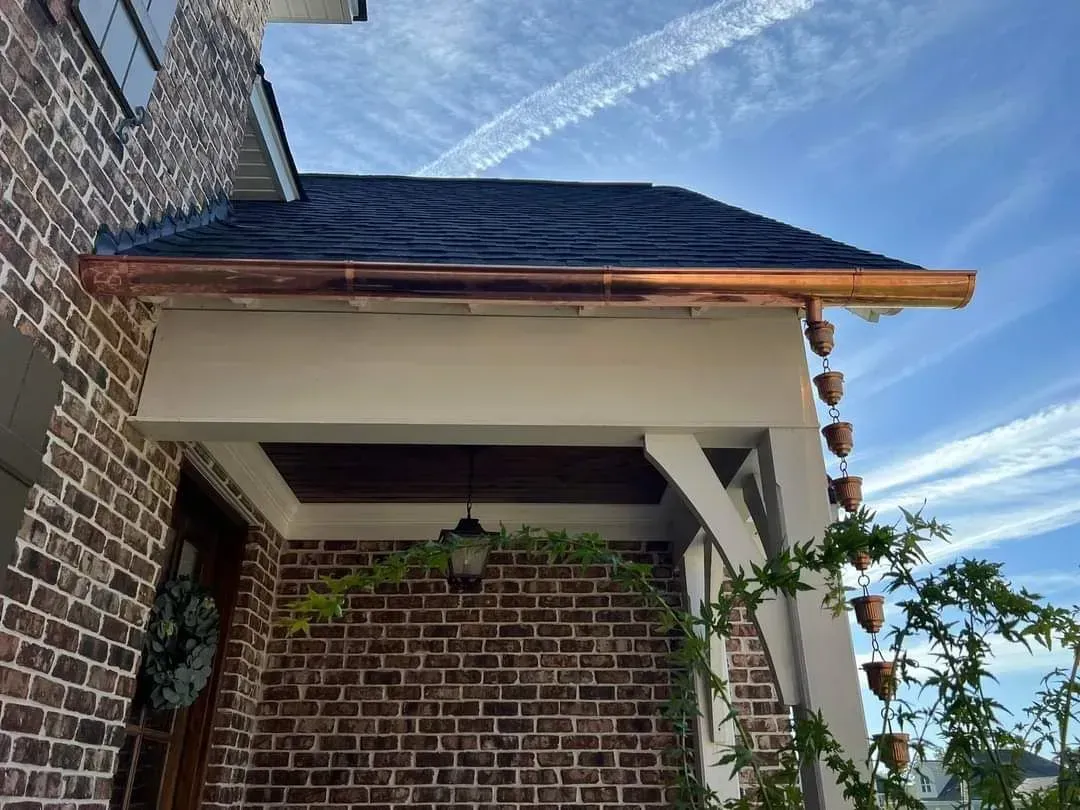 A brick house with a porch and a copper gutter on the roof.