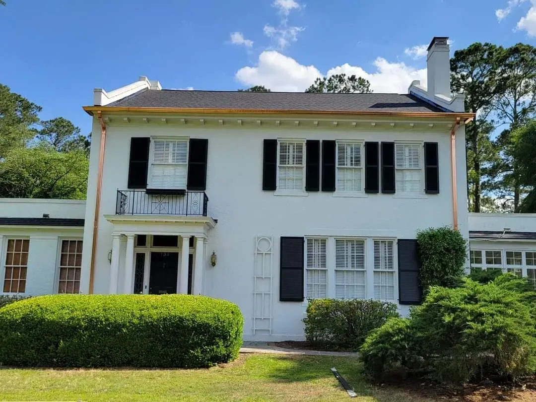 A large white house with black shutters and a copper gutter.