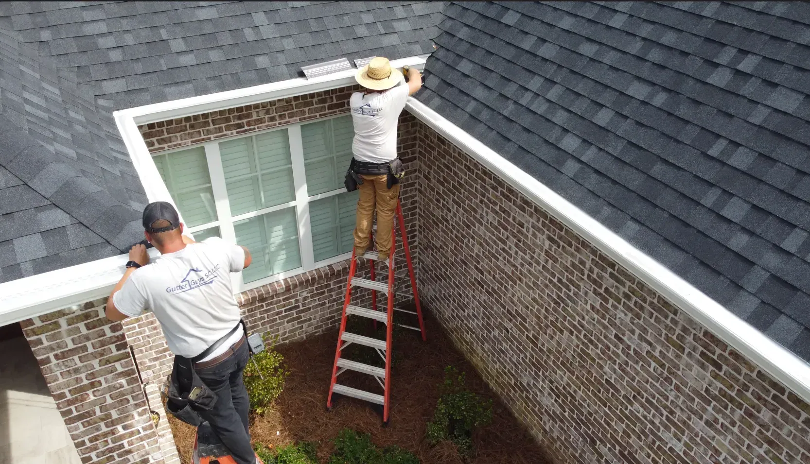 Two men are working on a gutter on the roof of a house.