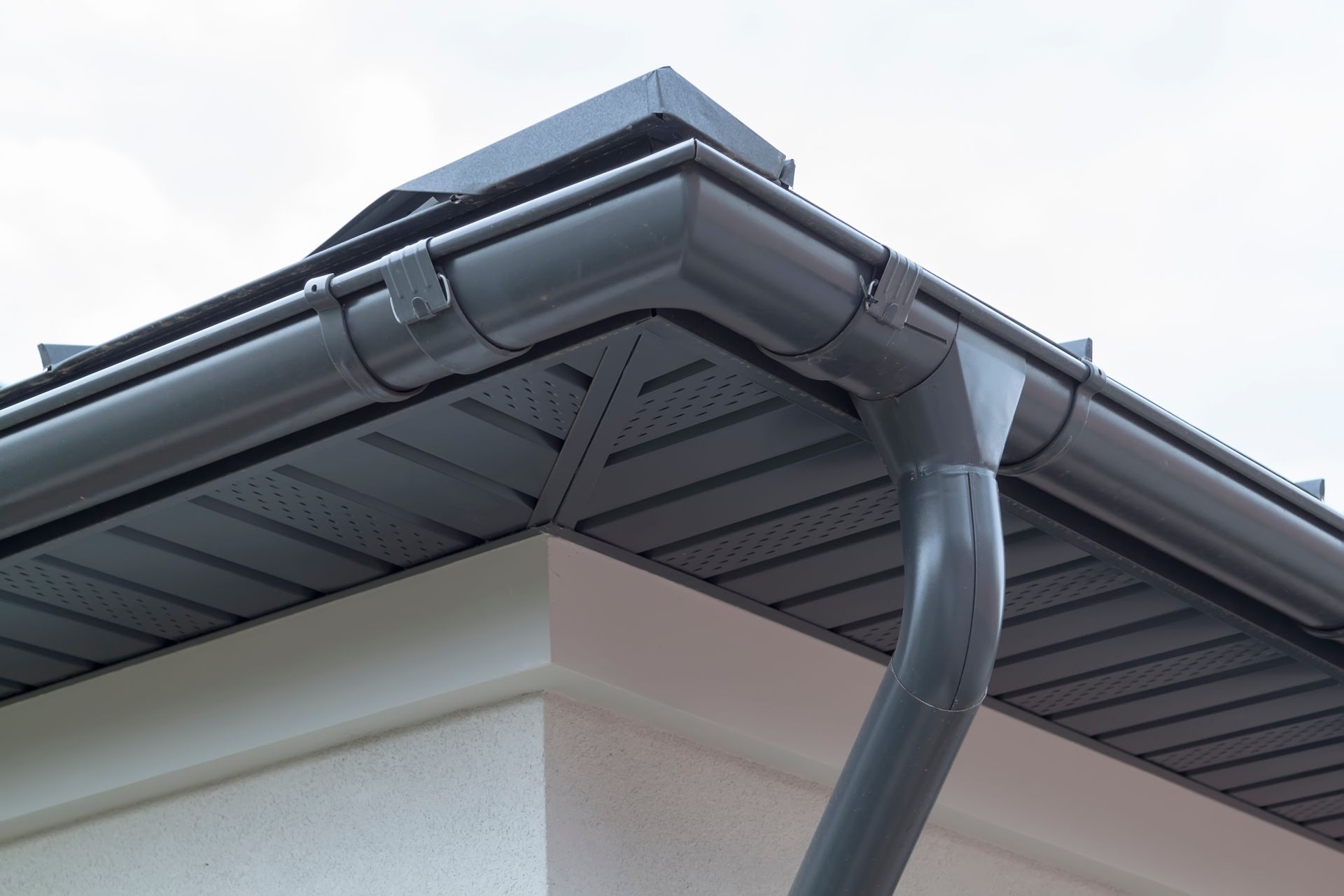 Close-up of gray rain gutters and downspout on a house roof corner