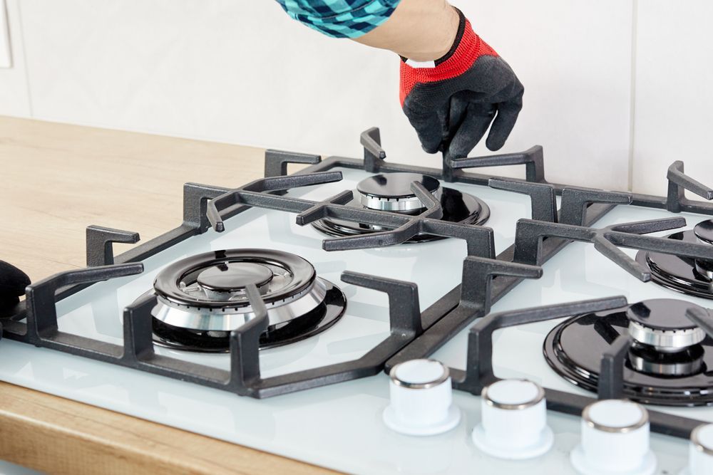 A Person is Fixing a Gas Stove in a Kitchen — Dave's Plumbing and Gasfitting in Maroochydore, QLD