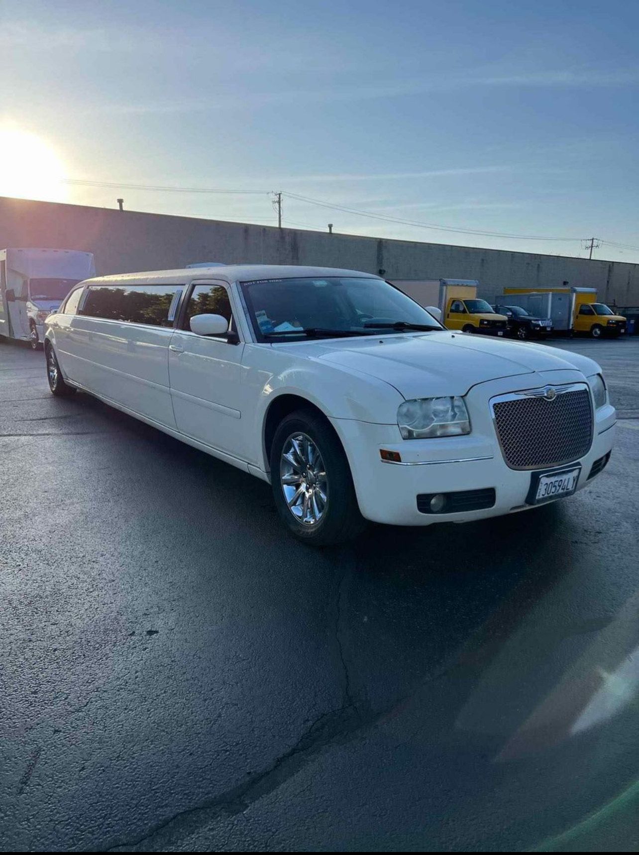 A white limousine is parked in a parking lot in front of a building.