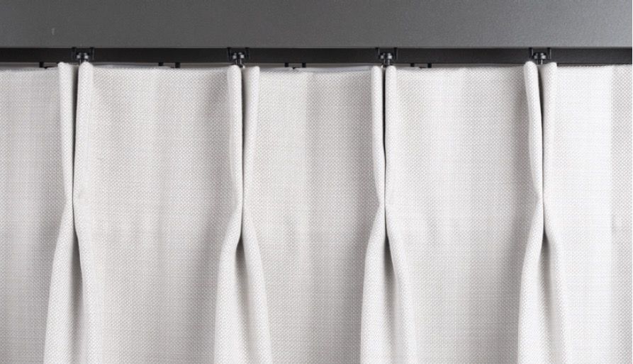 White pleated curtains hanging from a dark track.
