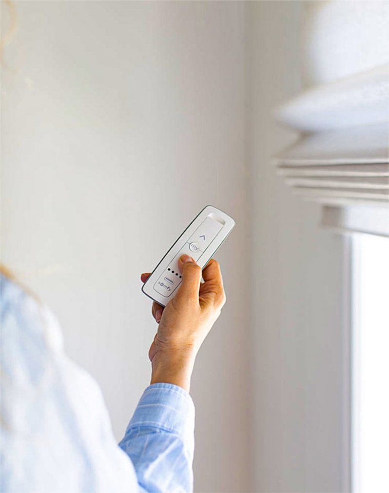A person is holding a remote control in front of a window.